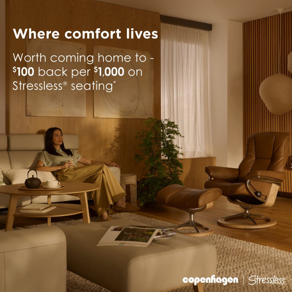 Photo of a woman relaxing in a sofa, looking up to the far top right of a living room. Previews the Stressless recliner to the right. Golden hour, mid day.